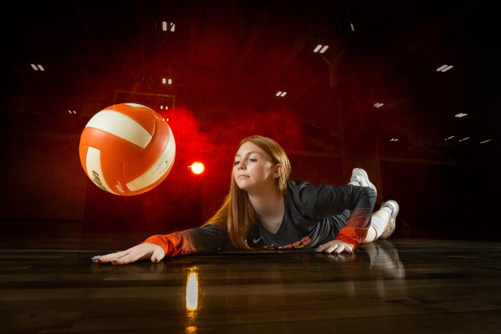 High school senior girl playing volleyball, diving to pancake the ball with dynamic lighting, captured by the best Kansas City senior photographer