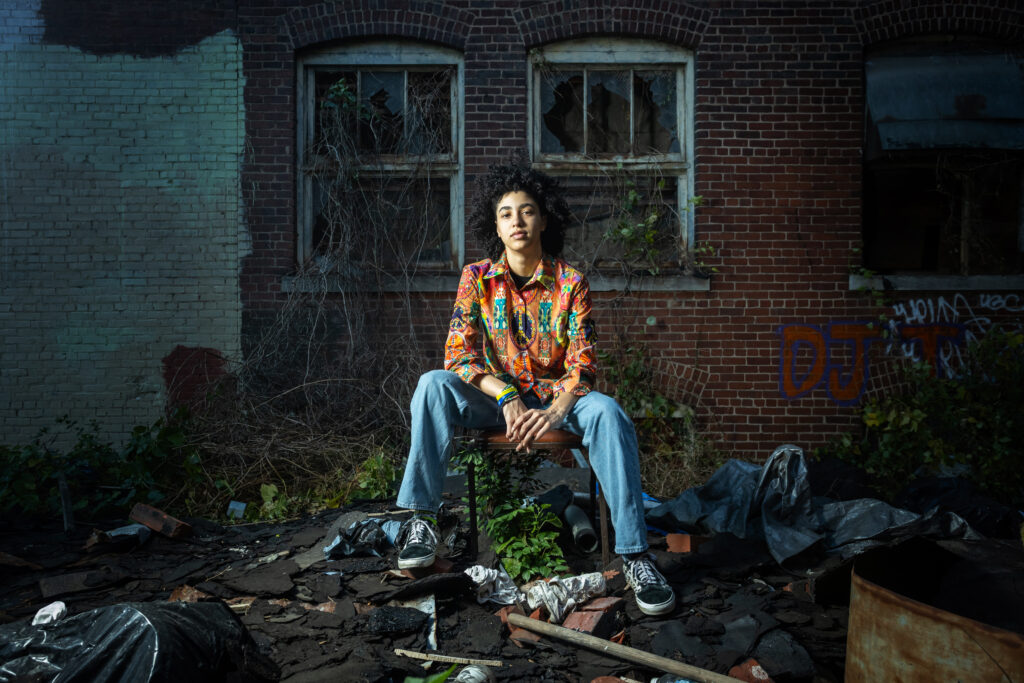 High school senior sitting in front of an abandoned building in the West Bottoms on a vacant lot with dramatic lighting, captured by a top Kansas City senior photographer.