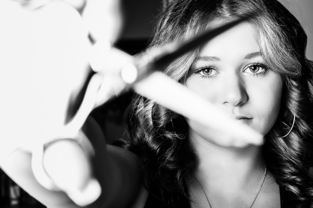 High school senior girl holding scissors in a cosmetology school, captured in black and white with a unique perspective by a top Kansas City senior photographer