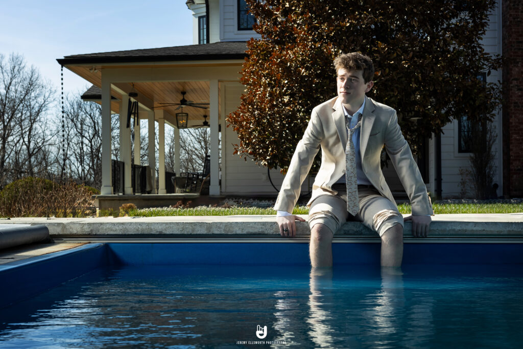 Platte County High school senior boy wearing a suit and sitting with his legs in a pool, captured by a creative Kansas City senior photographer during a unique portrait session.